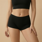 Person wearing black high-waisted shorts and a black crop top on a beige background