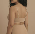 Woman wearing a beige bralette against a beige background
