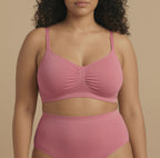 Woman wearing a pink bra and high-waisted underwear set against a beige background