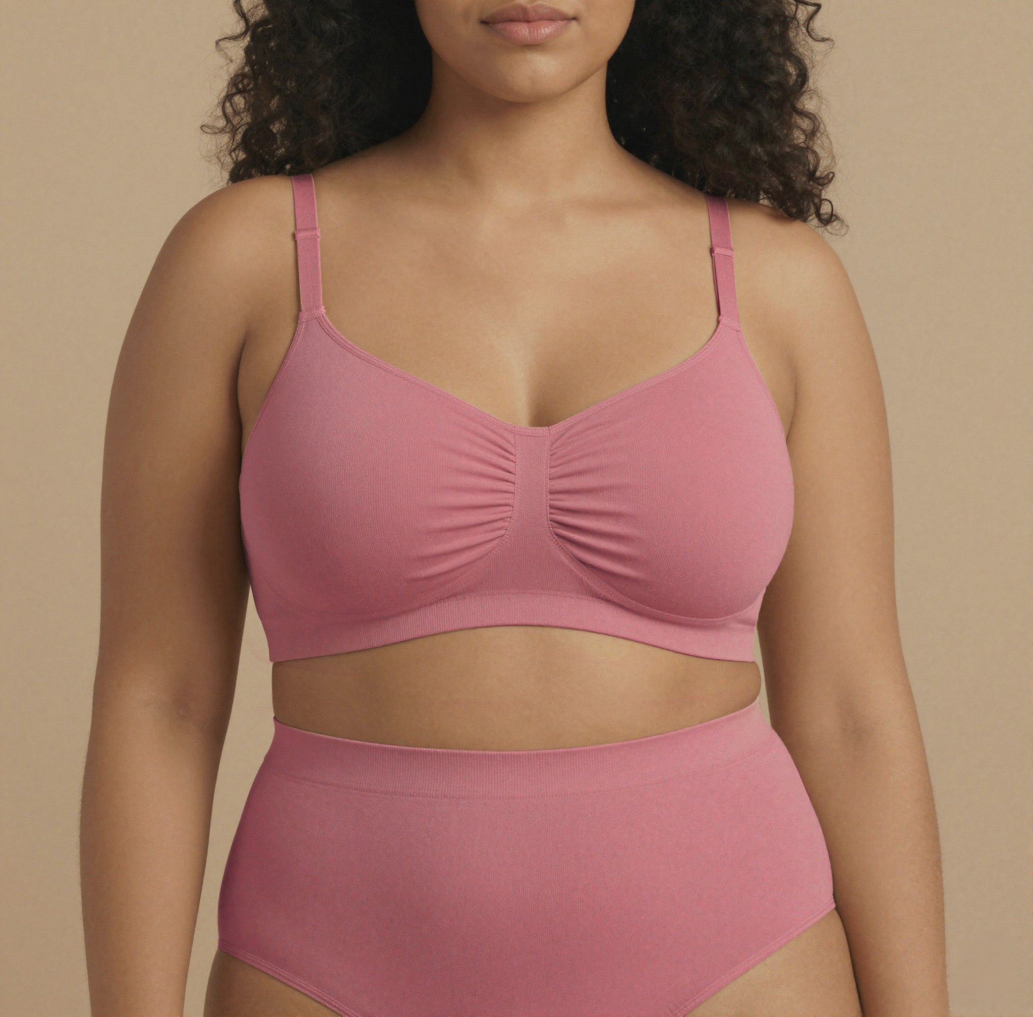 Woman wearing a pink bra and high-waisted underwear set against a beige background