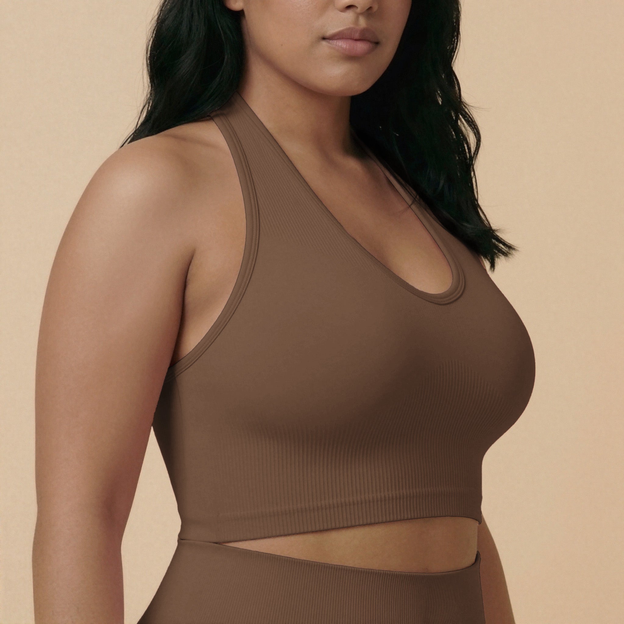 Woman wearing a brown sports bra and leggings against a beige background