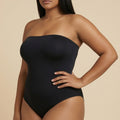 Woman wearing a black strapless swimsuit against a beige background